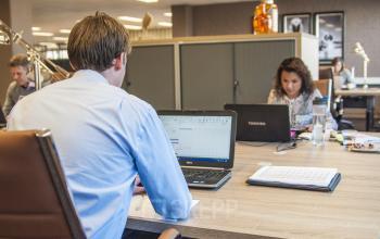 Professionals working on laptops in a furnished office space at Zaagmolenlaan 4, Woerden, with desks, chairs, and cabinets visible.