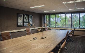 Modern conference room at Zaagmolenlaan 4 in Woerden, featuring a large wooden table, comfortable chairs, and ample natural light through large windows. Ideal office space rental for business meetings.