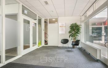 Entrance area of an office to rent at Huis ter Heideweg 24, Zeist, featuring carpeted flooring, seating, and glass partitions.
