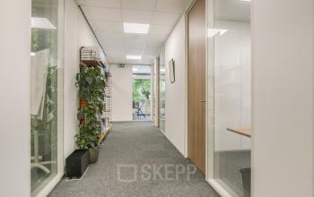 Interior hallway view of office space at Huis ter Heideweg 24, Zeist, showcasing carpeted floors, glass partitions, and several furnished workspaces. Ideal for those considering office space rental.