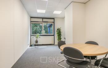 Bright office space available for rent at Huis ter Heideweg 24, Zeist, featuring a round table, chairs, and potted plants by a window.