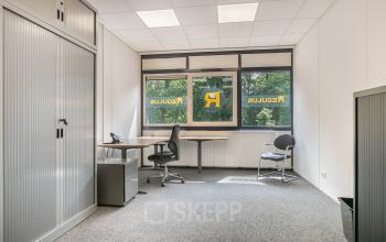 Well-lit office space for rent at Huis ter Heideweg 24, Zeist, featuring a desk, chairs, and a large window offering natural light.