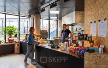 Modern office pantry at Boerhaavelaan 40, Zoetermeer, with two people interacting at the counter surrounded by snacks and beverages.
