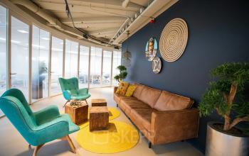 Inviting lounge area in an office with a brown sofa, two teal chairs, and decorative elements on the wall, located at Boerhaavelaan 40, Zoetermeer, offering office space rental options.