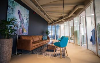 Office lounge area at Boerhaavelaan 40, Zoetermeer with modern seating, colorful art, and a curved wall with glass partitions.