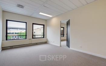 Interior view of an unfurnished office space available for rent on Edelgasstraat 101, Zoetermeer, featuring large windows with natural light and a neutral color palette.