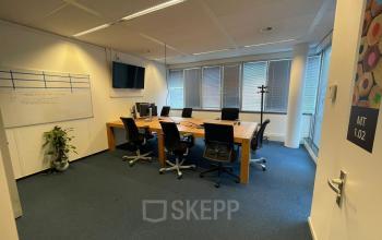 Modern conference room at Baron de Coubertinlaan 35, Zoetermeer, featuring a large wooden table, office chairs, a whiteboard, and a flat-screen TV, ideal for office space rental.