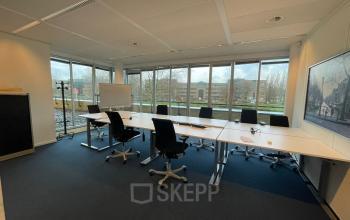 Spacious office to rent at Baron de Coubertinlaan 35, Zoetermeer, featuring a large table with chairs, ready for meetings. Ideal for office space rental with expansive windows letting in natural light.
