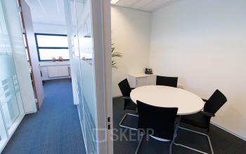 Interior view of office space for rent at Louis Braillelaan 80, Zoetermeer, featuring a glass-walled room with a round table and chairs.