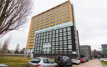 Exterior view of the office building located at Louis Braillelaan 80 in Zoetermeer. Several parked cars can be seen in front of the yellow and black multi-story building.