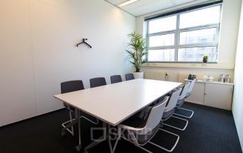 Modern conference room for office space rental at Louis Braillelaan 80, Zoetermeer, featuring a large table, chairs, plants, and ample natural light from windows.