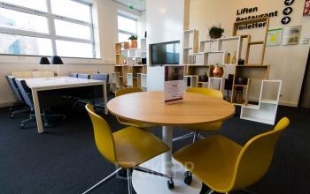 Modern office space at Louis Braillelaan 80, Zoetermeer with round table, yellow chairs, bookshelf, and large windows providing natural light.