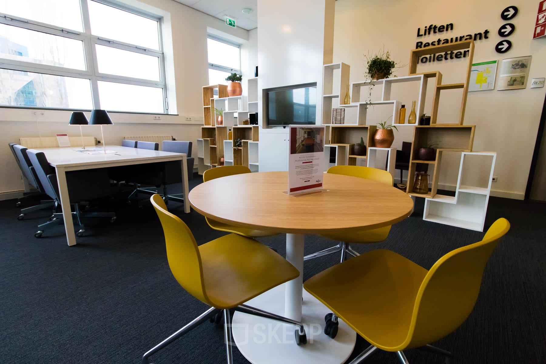 Modern office space at Louis Braillelaan 80, Zoetermeer with round table, yellow chairs, bookshelf, and large windows providing natural light.