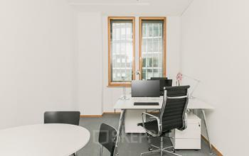 Streamlined office space rental at The Circle, Zürich Airport, featuring a tidy desk with computer and a round meeting table.