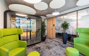 Moderne Bürofläche in Zürich Seebach, Thurgauerstrasse 132, mit grünen Sesseln und einem Besprechungspod.