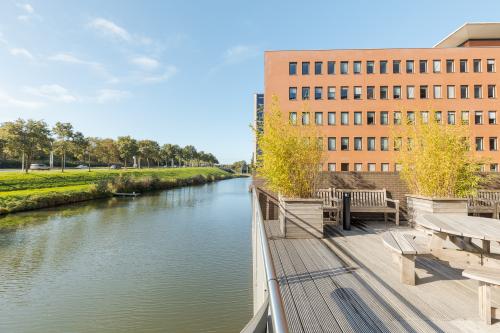 Exterior view of the office building at Zuiderzeelaan 27-41 in Zwolle, featuring a waterside terrace with wooden seating, surrounded by greenery, ideal for office space rental.