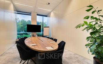Conference room at Zwartewaterallee 56, Zwolle, featuring a sleek, oval wooden table and comfortable chairs, ideal for meetings. Large window provides natural light while greenery enhances the atmosphere. Perfect for office space rental.