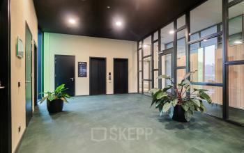 Modern entrance at Zwartewaterallee 56 in Zwolle, featuring sleek glass walls and vibrant green plants, ideal for those seeking office space rental with a contemporary touch.