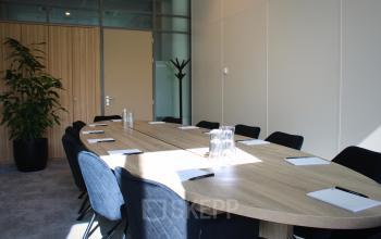 Modern conference room with a large wooden table, black chairs, and note pads set up for a meeting at Zwartewaterallee 56, Zwolle.