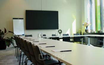 Modern conference room with a long white table, chairs, a large screen, and a flip chart at Zwartewaterallee 56, Zwolle.