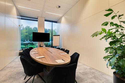 Conference room at Zwartewaterallee 56, Zwolle, featuring a sleek, oval wooden table and comfortable chairs, ideal for meetings. Large window provides natural light while greenery enhances the atmosphere. Perfect for office space rental.