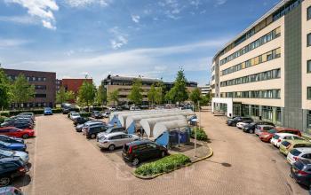 A parking lot filled with cars outside an office building on Dokter van Deenweg 1 in Zwolle, ideal for office space rental.