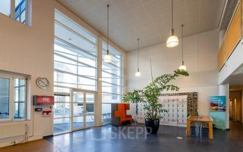 Bright and open office entrance with high ceilings, large windows, and a seating area, ideal for an inviting office space rental.