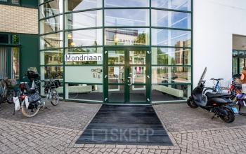 Exterior view of an office building at Dokter van Deenweg 1, Zwolle, highlighting the entrance with glass facades and a mix of bikes and scooters parked outside.