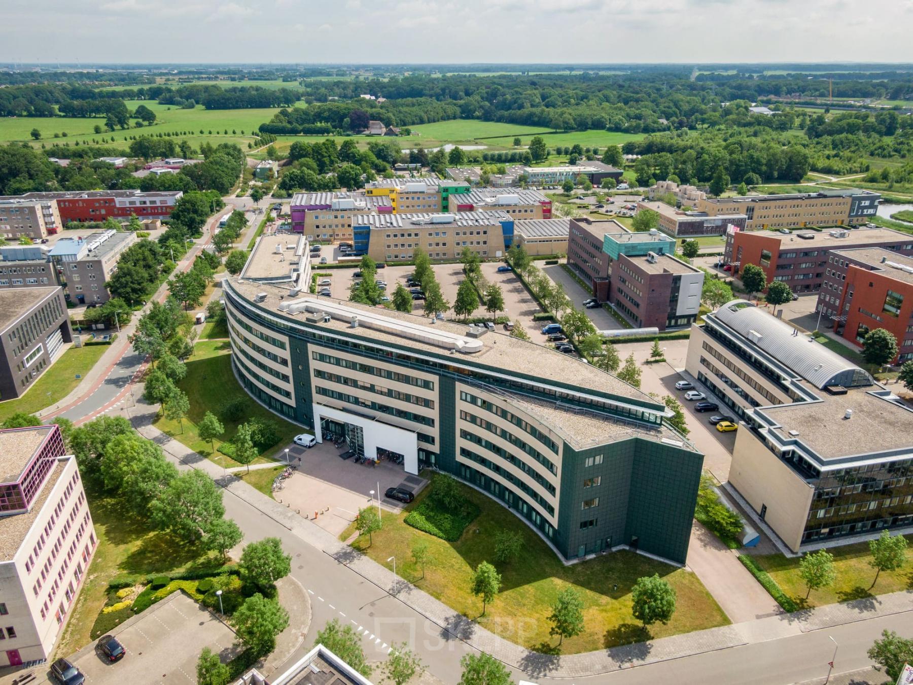 Aerial view of a modern office building at Dokter van Deenweg 1, Zwolle, ideal for office space rental, surrounded by greenery and other commercial buildings.