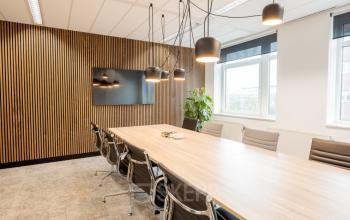 Modern conference room with a long wooden table, sleek chairs, and ambient lighting at Zuiderzeelaan 15-25, Zwolle. Perfect for office space rental with a professional and inviting atmosphere.