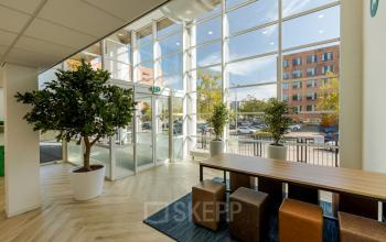 Bright office space at Zuiderzeelaan 15-25, Zwolle, featuring stylish furniture including a long table and cube chairs, ideal for informal meetings. Large windows allow natural light to enhance the inviting space.