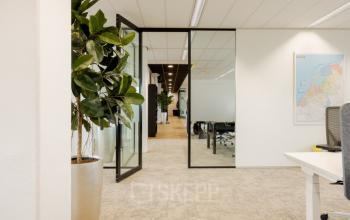 Modern office interior at Zuiderzeelaan 15-25, Zwolle, featuring glass doors and carpeted floors, ideal for office space rental. The room includes seating and plants, creating a professional and inviting atmosphere.