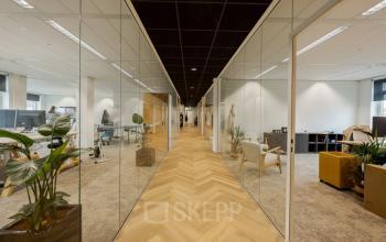 Spacious office space rental at Zuiderzeelaan 15-25 in Zwolle featuring modern furnishings, polished wooden floors, and an open-floor plan with glass partitions and plants for a conducive work environment.
