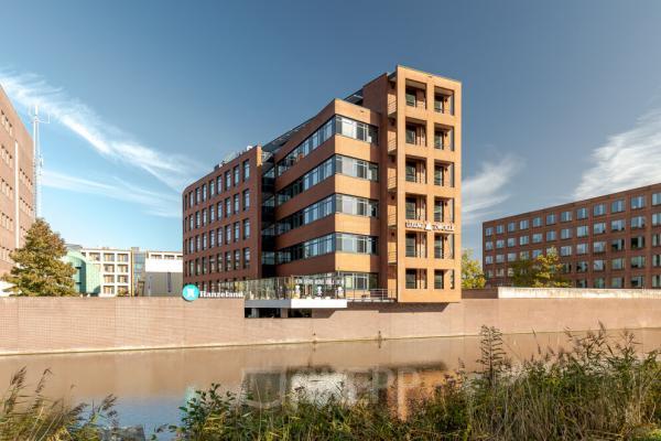 View of a modern office building located at Zuiderzeelaan 15-25, Zwolle, featuring glass windows and near a canal, ideal for office space rental.